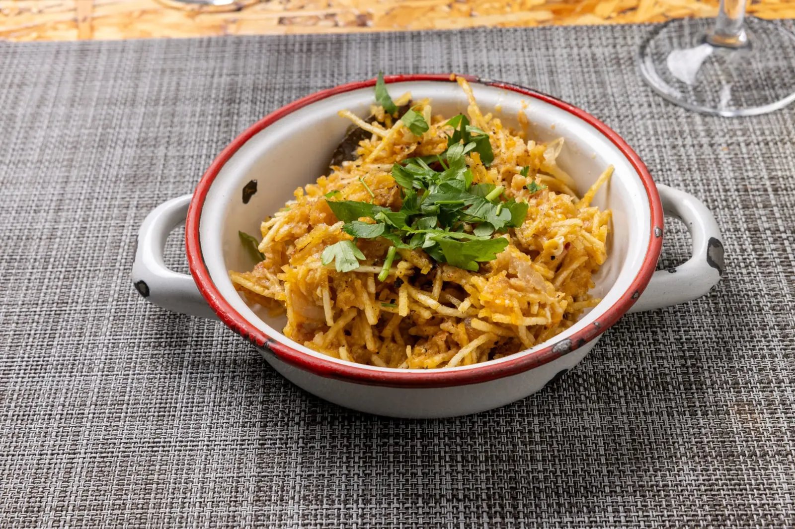 Bowl of golden shredded food garnished with green herbs on a gray woven placemat.