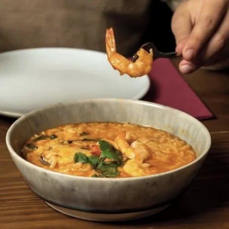 Bowl of orange shrimp soup garnished with herbs, with a fork holding a shrimp above it.