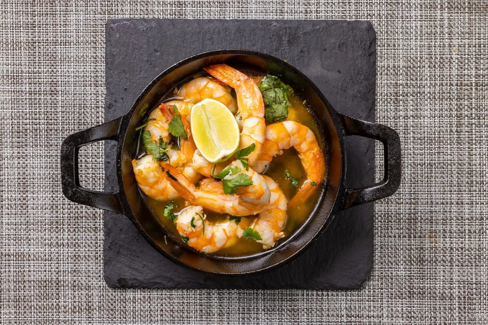 Shrimp with lime and cilantro in a cast-iron skillet on a slate board.