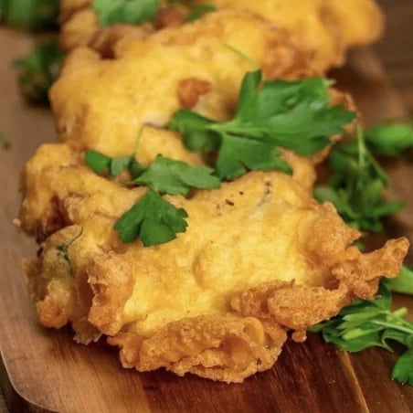 Golden battered fried pieces garnished with parsley on a wooden board.